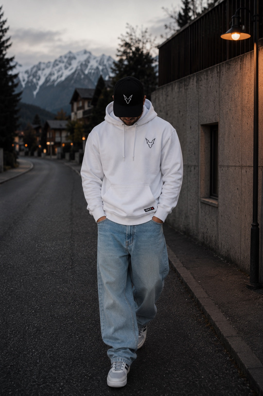 Model wearing an oversized white IBEX hoodie in a Swiss alpine street setting